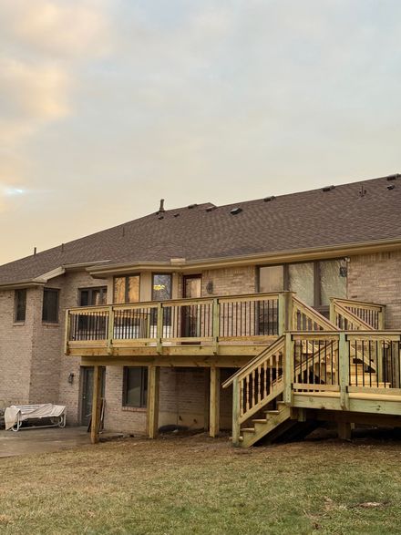 Backyard deck attached to a two-story stone house at sunset, with stairs and a small lawn