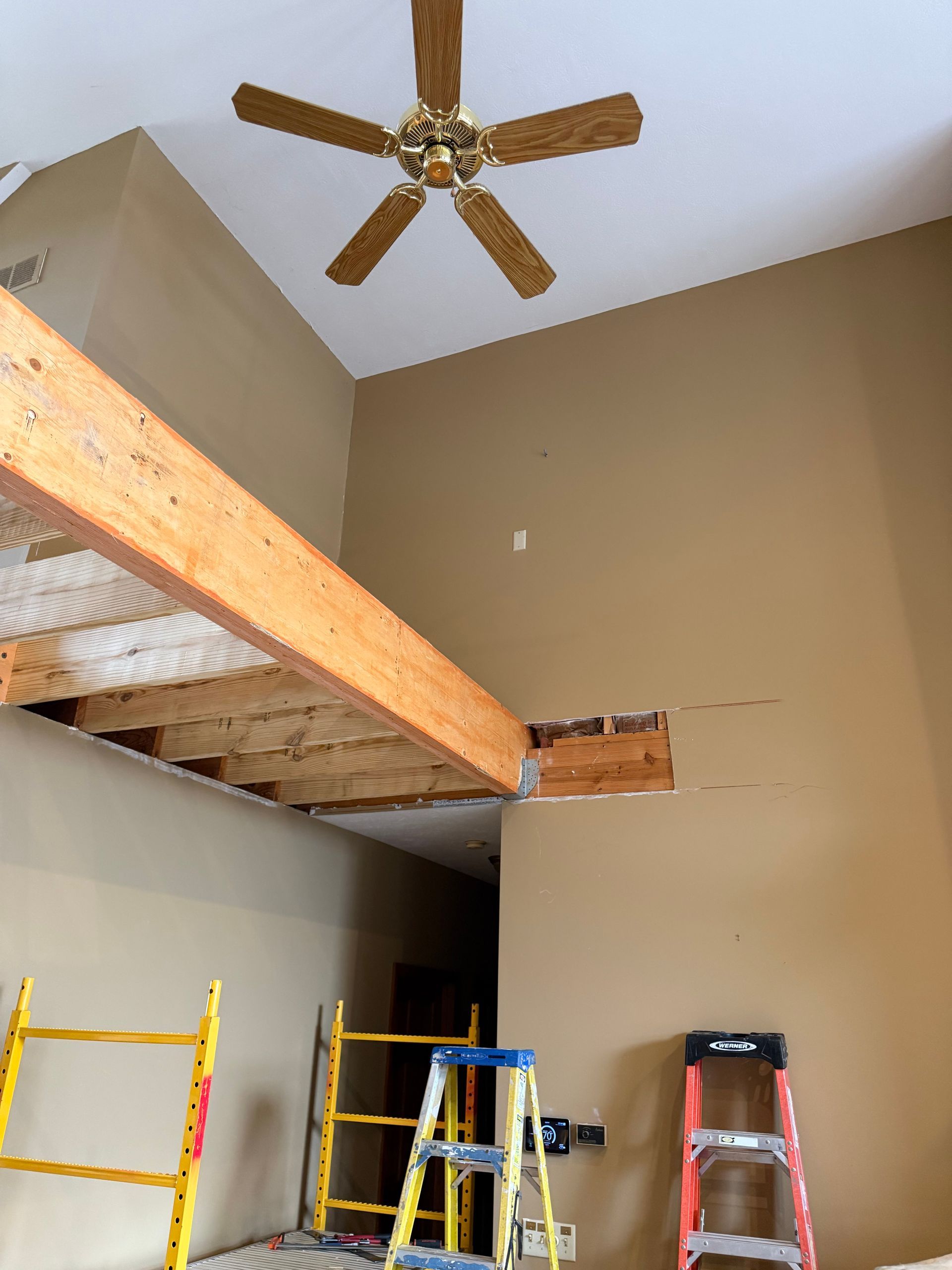 High-ceiling room with a loft and ladders, tan walls, and a ceiling fan above.