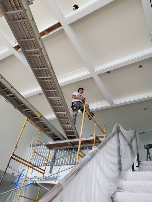 Worker on scaffolding inside a white stairwell, installing or inspecting the ceiling.