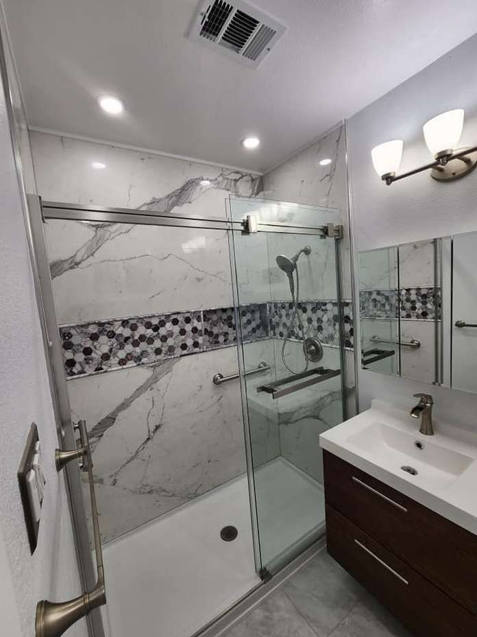 Bathroom with a white marble-patterned shower, glass door, dark wood vanity, and a mosaic tile accent.