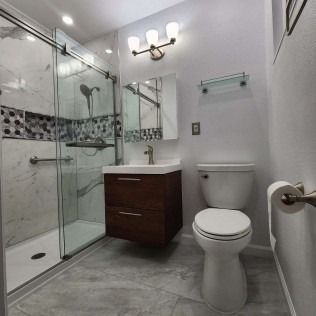 Modern bathroom with walk-in shower, floating vanity, and toilet. Gray tile floor and white walls.