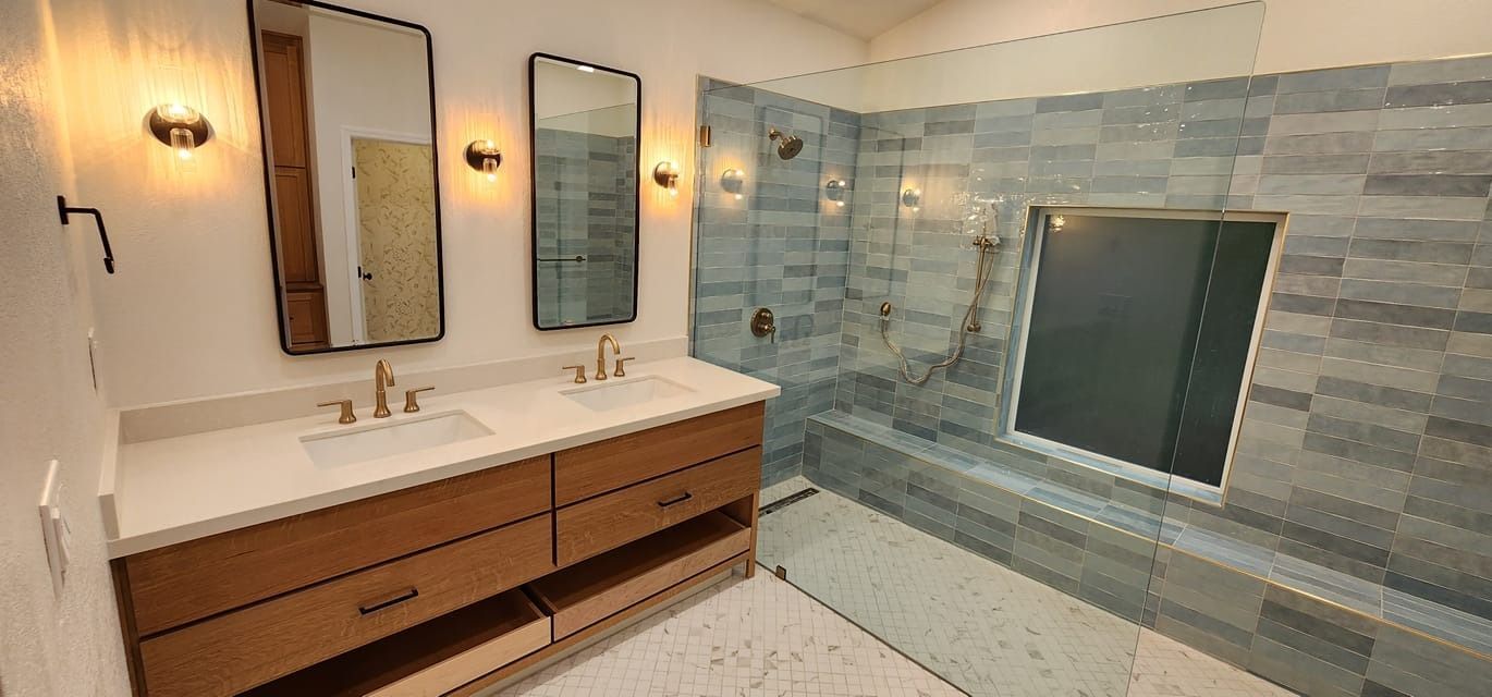 Bathroom with dual sinks, mirrors, and a tiled walk-in shower. Natural wood vanity, neutral colors.