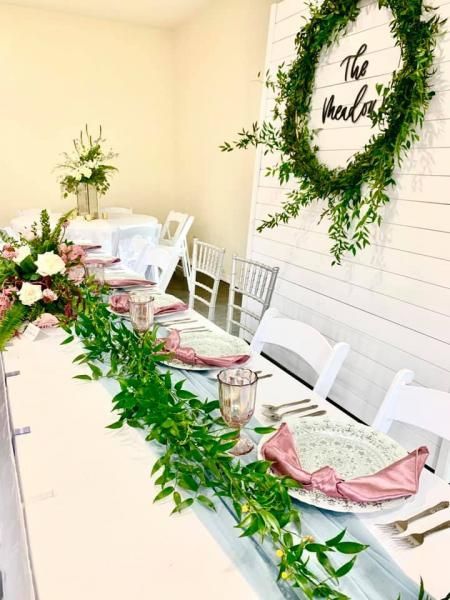 Decorated long banquet table with white chairs, pink napkins, greenery, and a leafy wall sign reading “The Walker”