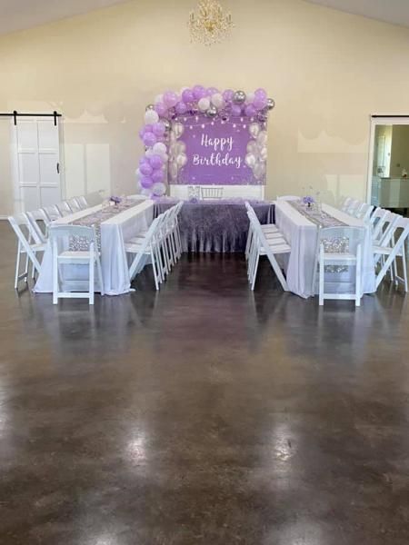 Purple balloon birthday backdrop between white tables and chairs in a decorated event hall