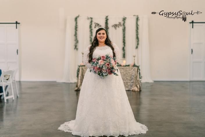 Bride holding bouquet in a white wedding dress, standing in a decorated indoor venue.