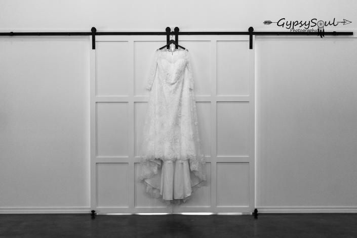 White wedding dress hanging on a wall-mounted rail in a minimalist room