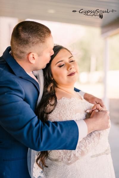 Couple embracing in a softly lit wedding portrait, the woman in a white lace dress and the man in a blue suit