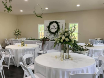 White round tables and chairs in a decorated reception hall with floral centerpieces and greenery centerpiece backdrop