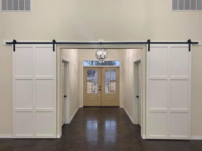 White sliding barn doors frame a hallway with double glass doors and a wall clock at the far end.