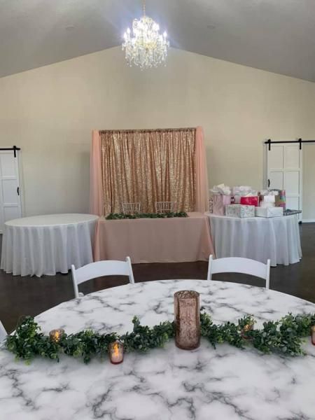 Decorated event room with white tables, greenery garland, candle, and peach draped backdrop under a chandelier