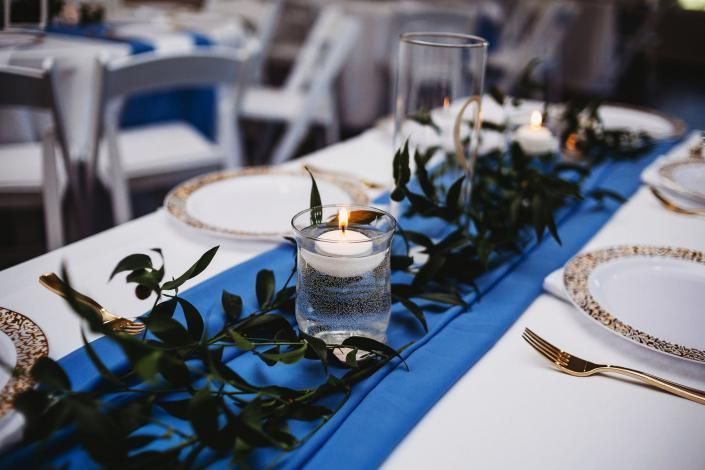 Elegant table setting with blue runner, greenery, candles, and gold-rimmed plates