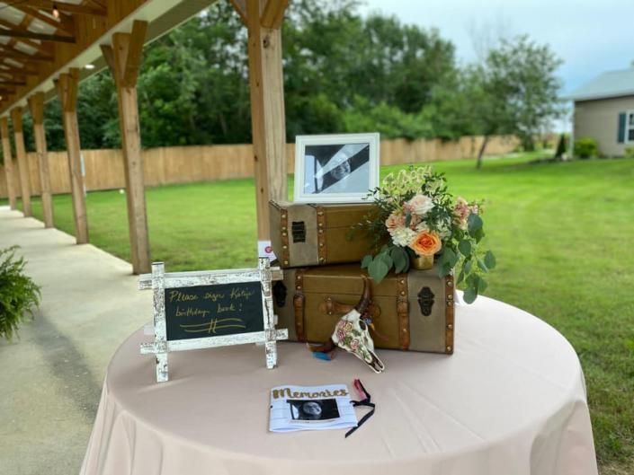 Outdoor memorial table with framed photos, flowers, and candles under a wooden pavilion.