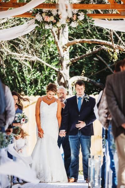 Wedding couple walking down an outdoor aisle under white drapes and trees