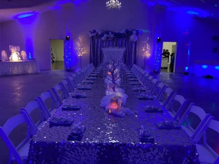 Blue-lit banquet hall with long decorated dining tables and chairs arranged for an event