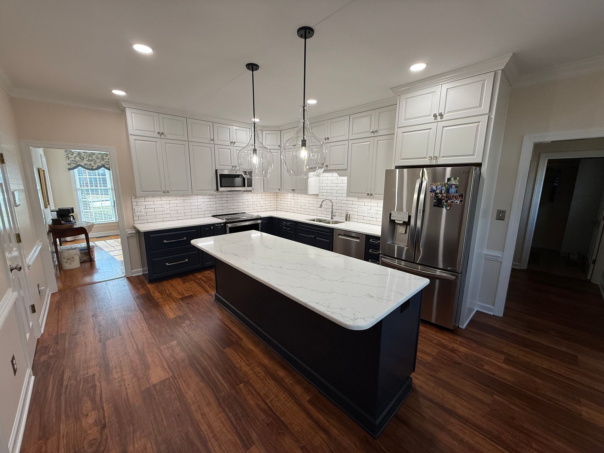 Modern kitchen with dark wood floors, white cabinets, navy island, and stainless steel appliances.