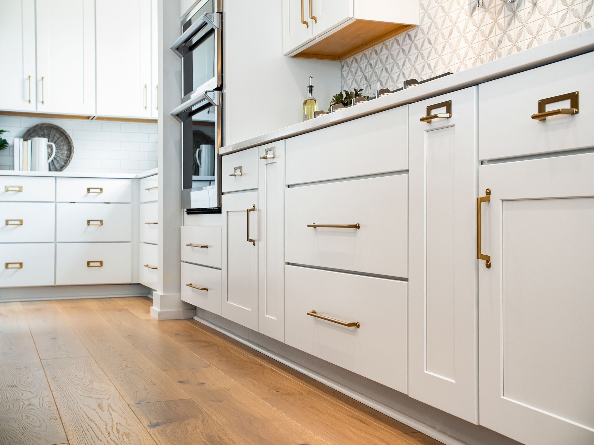 White kitchen cabinets with brass hardware, wooden floor.