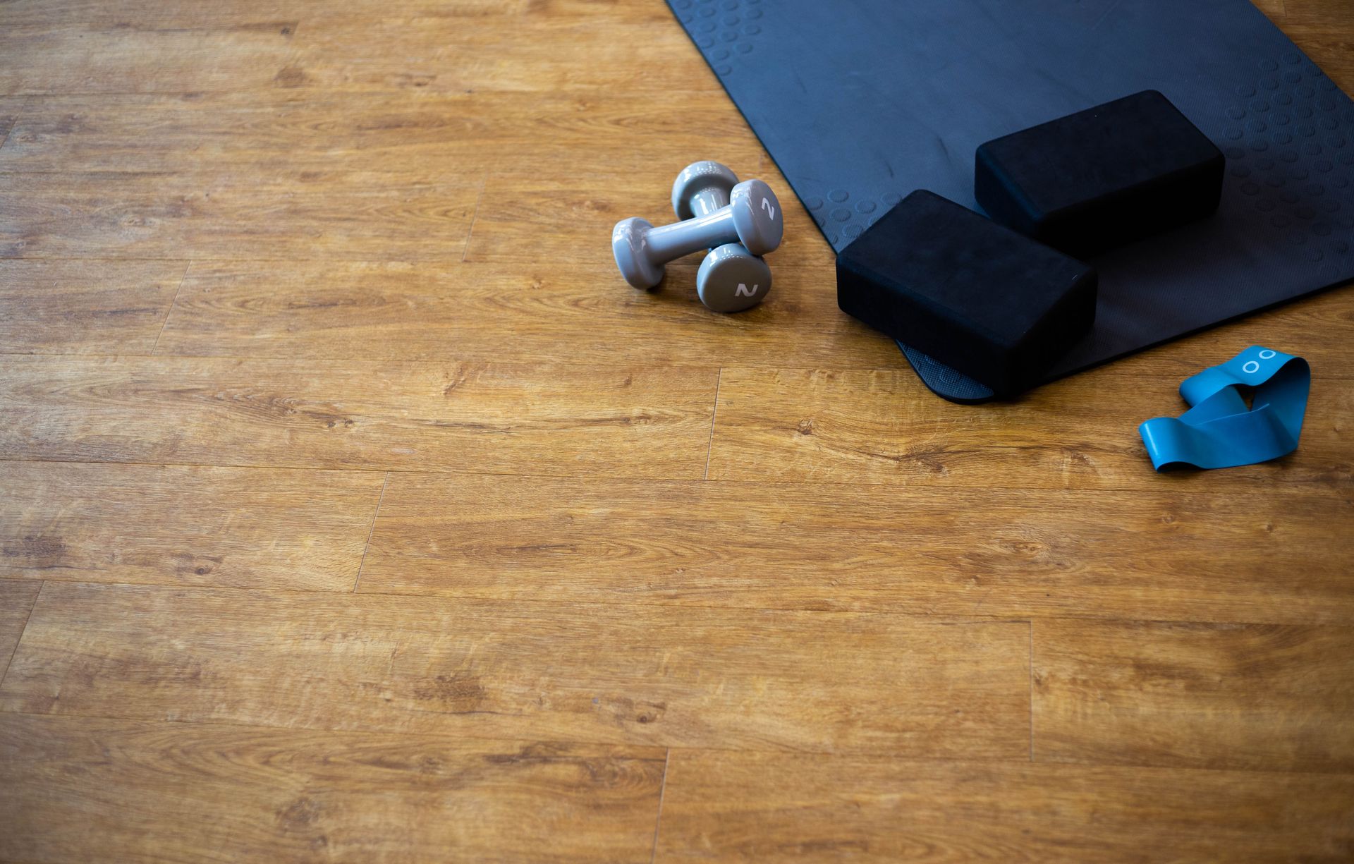 Blue yoga mat with dumbbells and a resistance band on a wooden floor