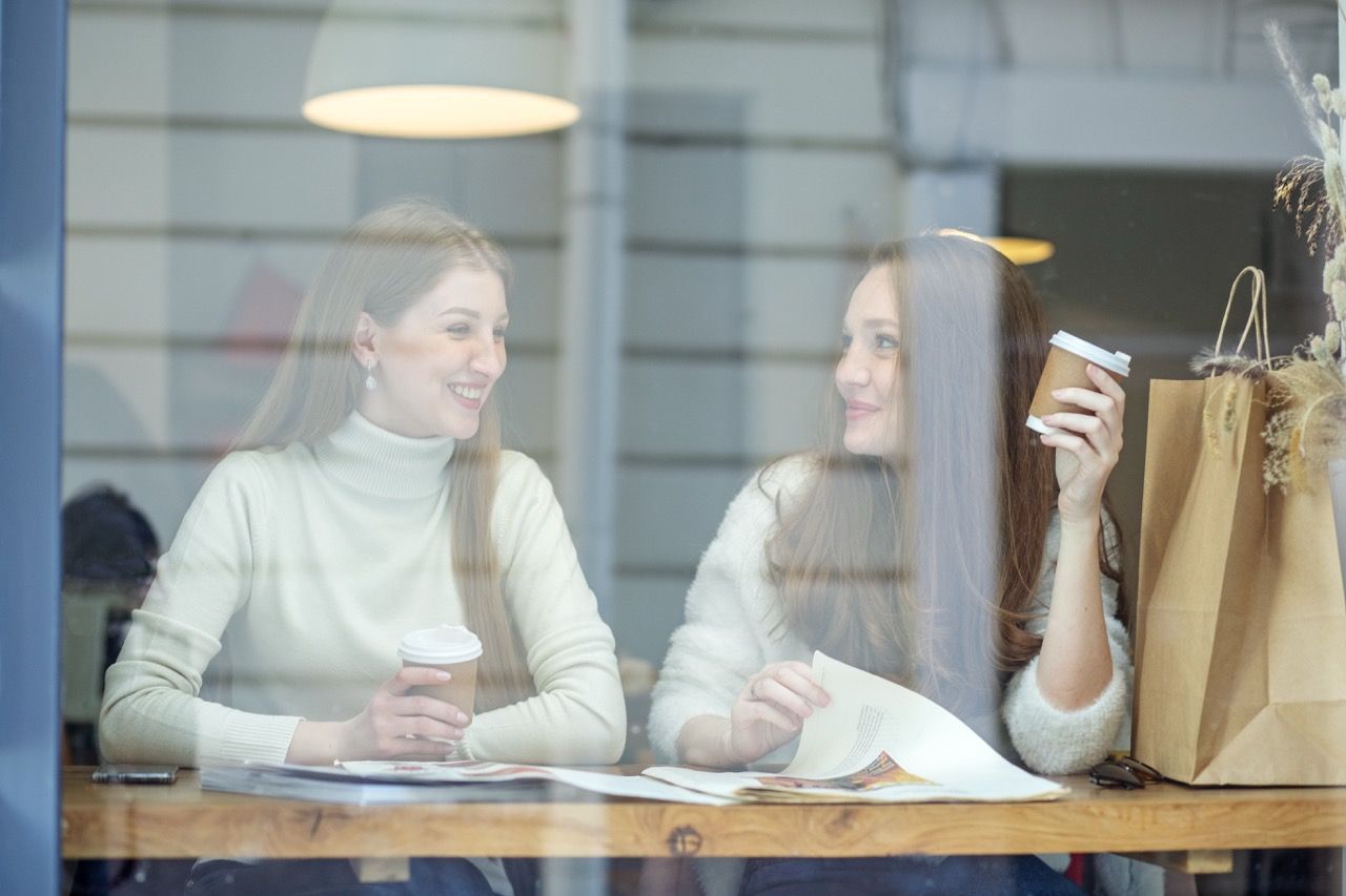 Two people talking at a café table, smiling with shopping bags beside them