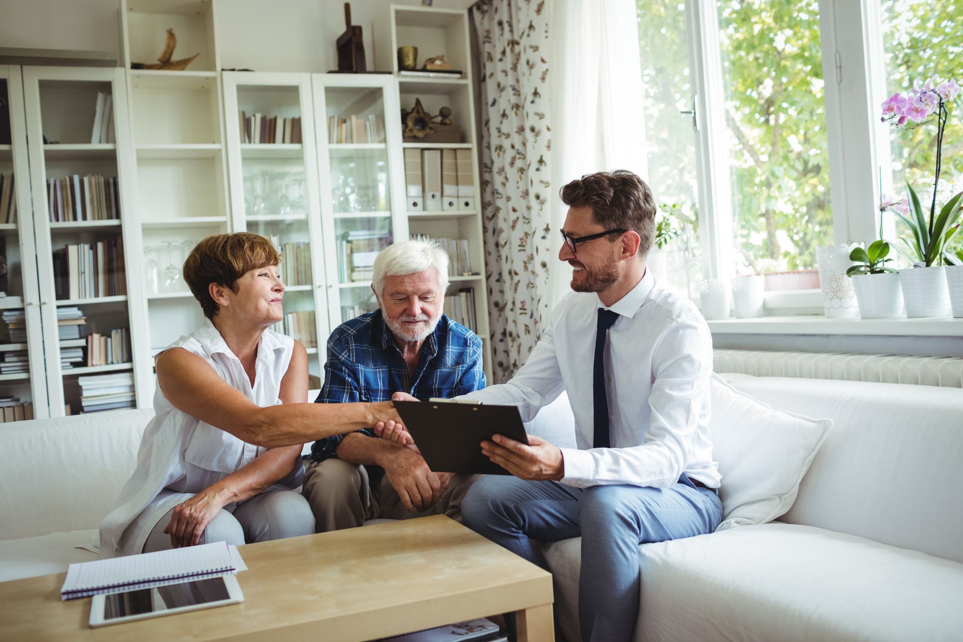 Three people discussing a document on a couch in a bright living room with a laptop on the table.