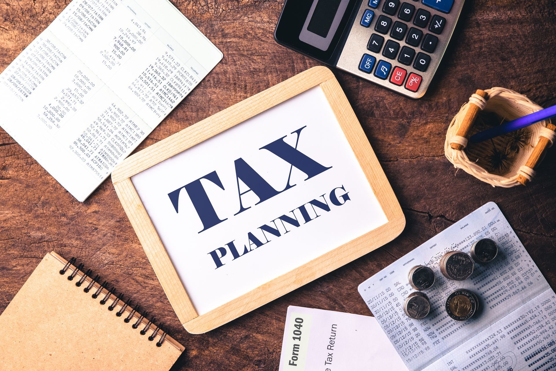 Tax planning materials on a wooden desk with calculator, notebook, papers, and pen.