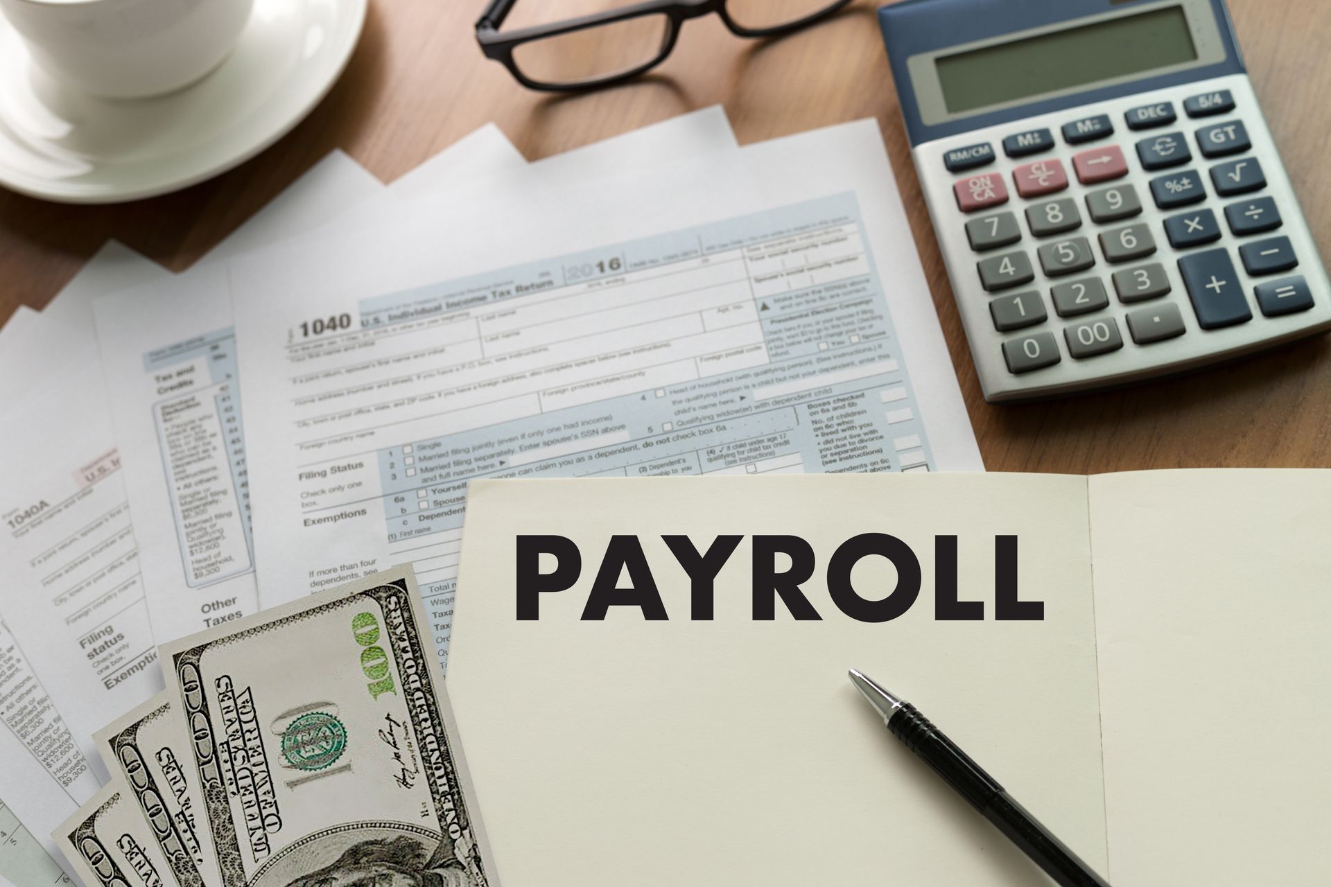Payroll documents, calculator, cash, and pen on a desk with a coffee cup