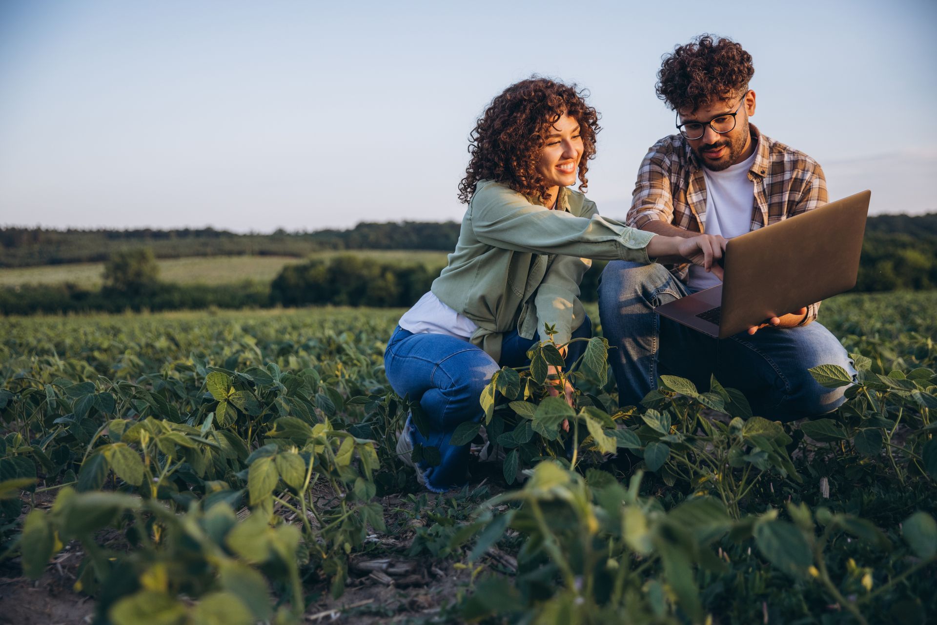 Two people kneeling in a field, looking at a laptop together under warm sunlight. Two people kneeling in a field, looking at a laptop together under warm sunlight.