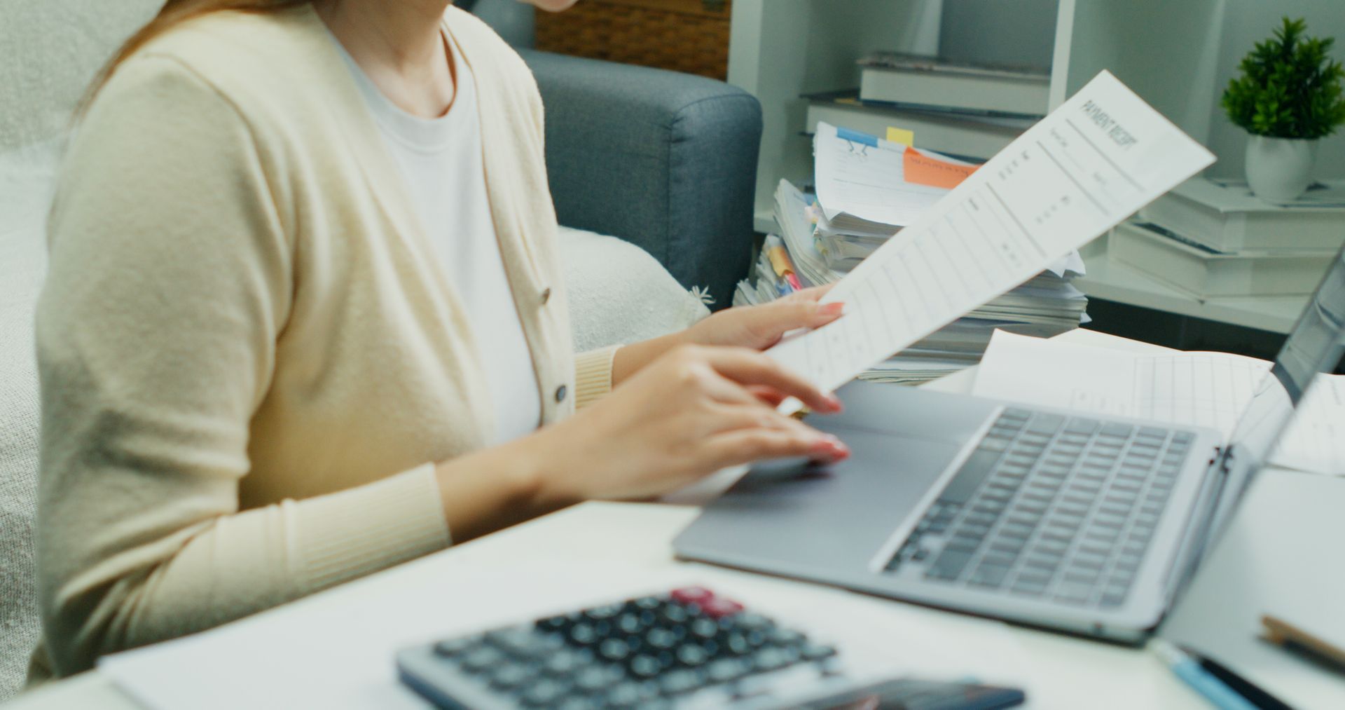 Person reviewing documents at a desk with a laptop and calculator in a bright office Person reviewing documents at a desk with a laptop and calculator in a bright office