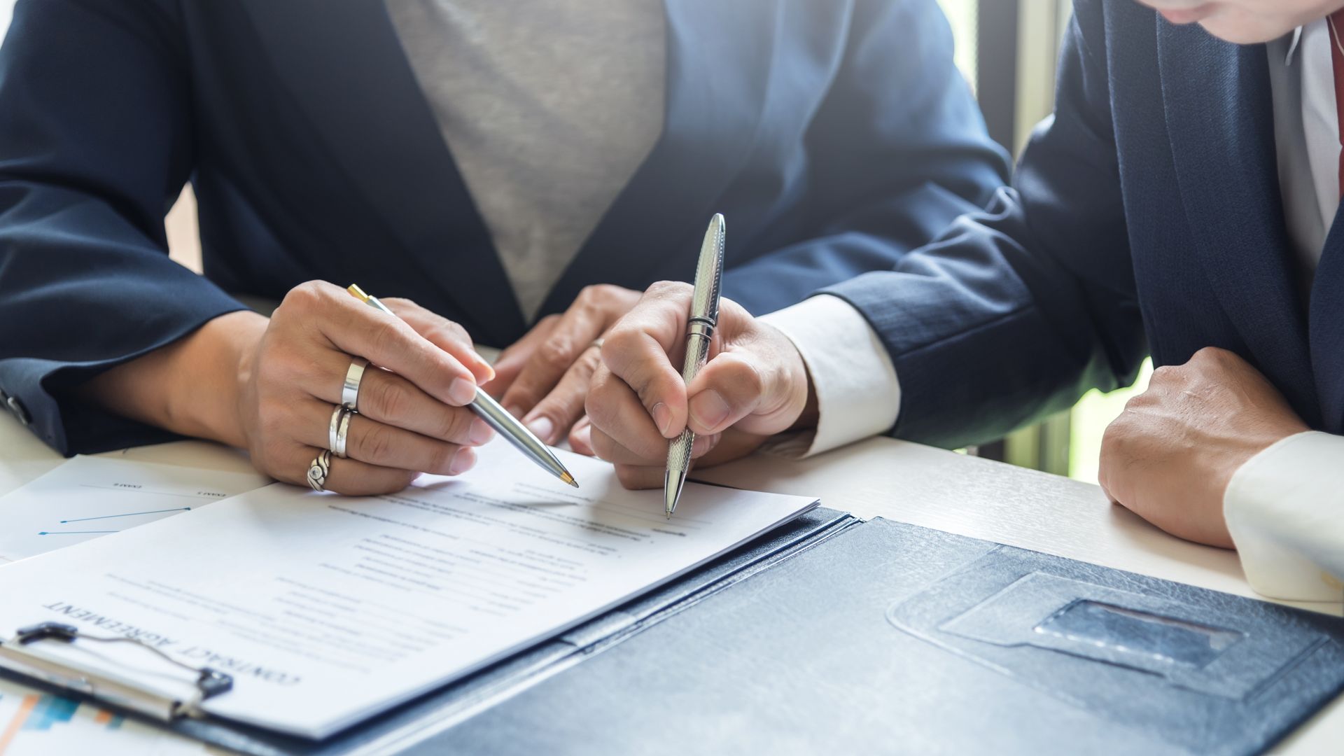Two people signing documents at a table with a laptop nearby