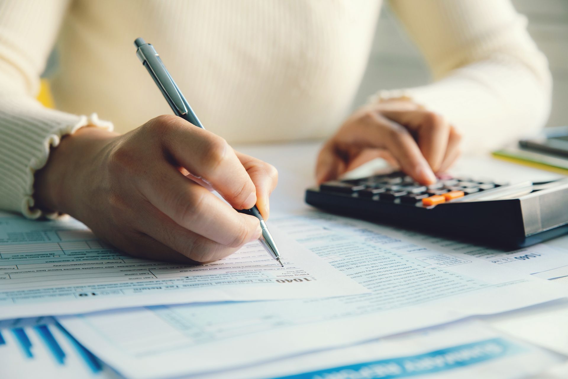 Hands writing on paperwork beside a calculator on a desk Hands writing on paperwork beside a calculator on a desk