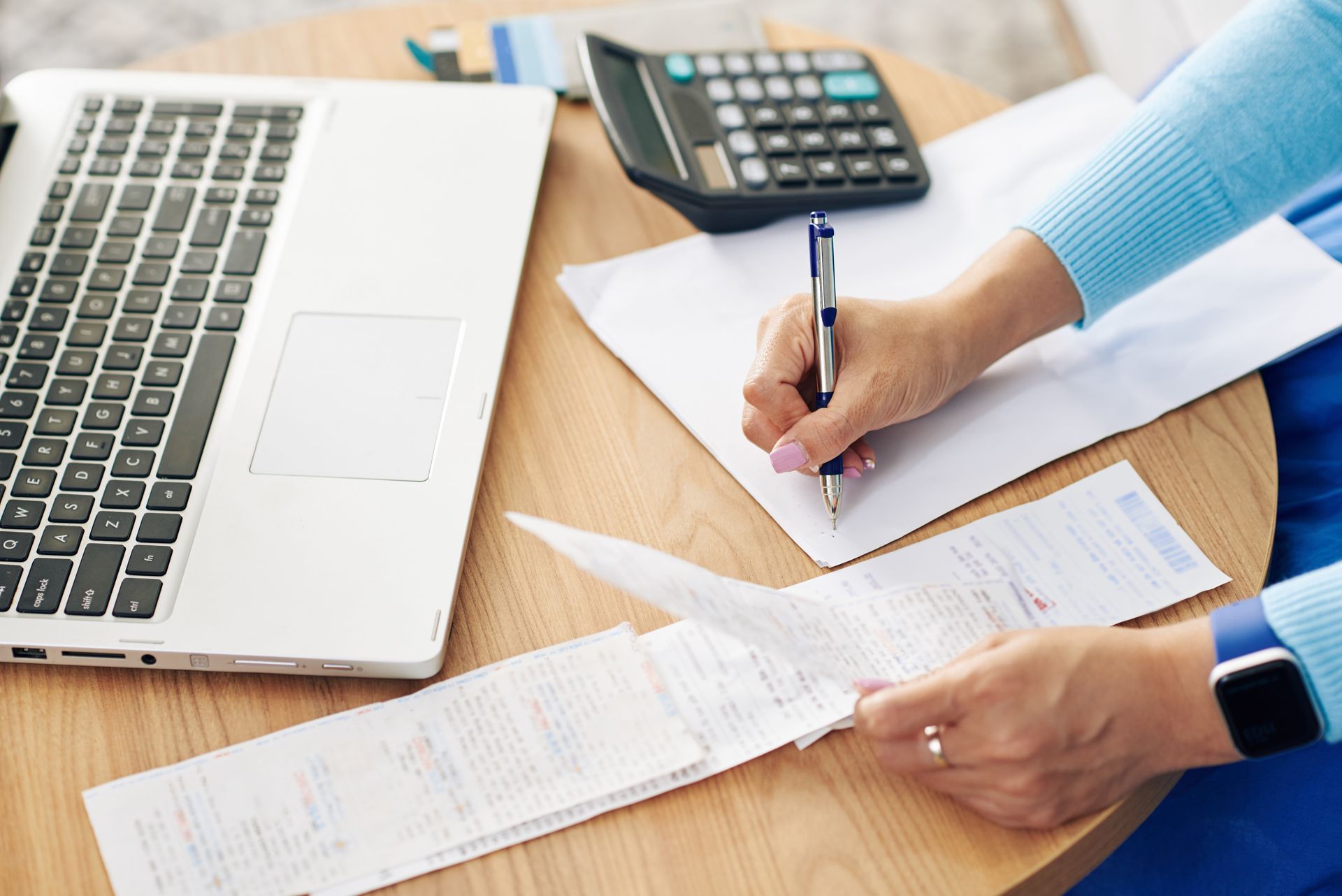 Hands reviewing documents beside a laptop and calculator on a desk