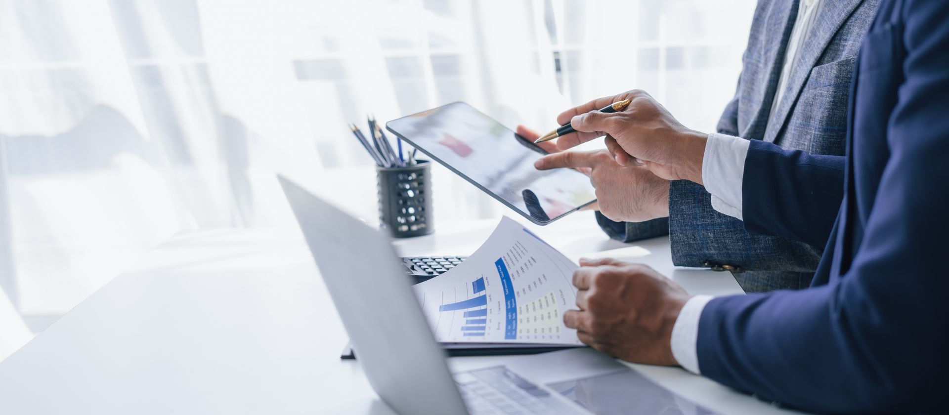 Person analyzing charts on a tablet beside a laptop in a bright office Person analyzing charts on a tablet beside a laptop in a bright office