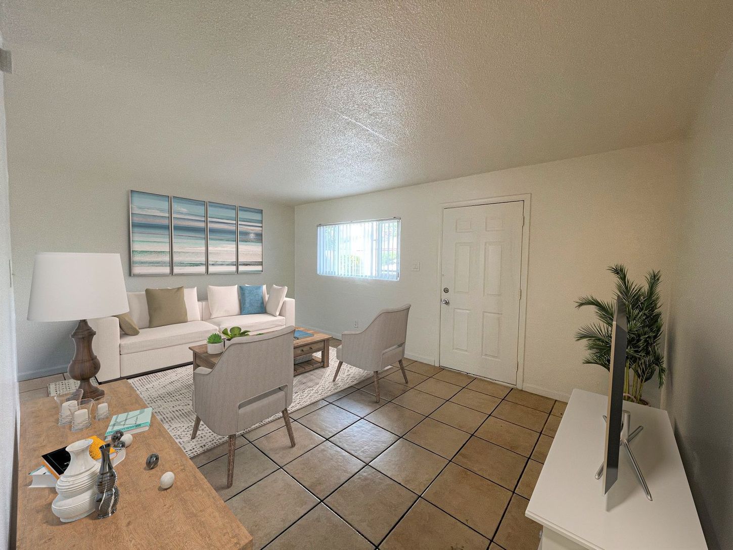 Living room with white walls, beige tile floor, sofa, chairs, TV, and artwork.