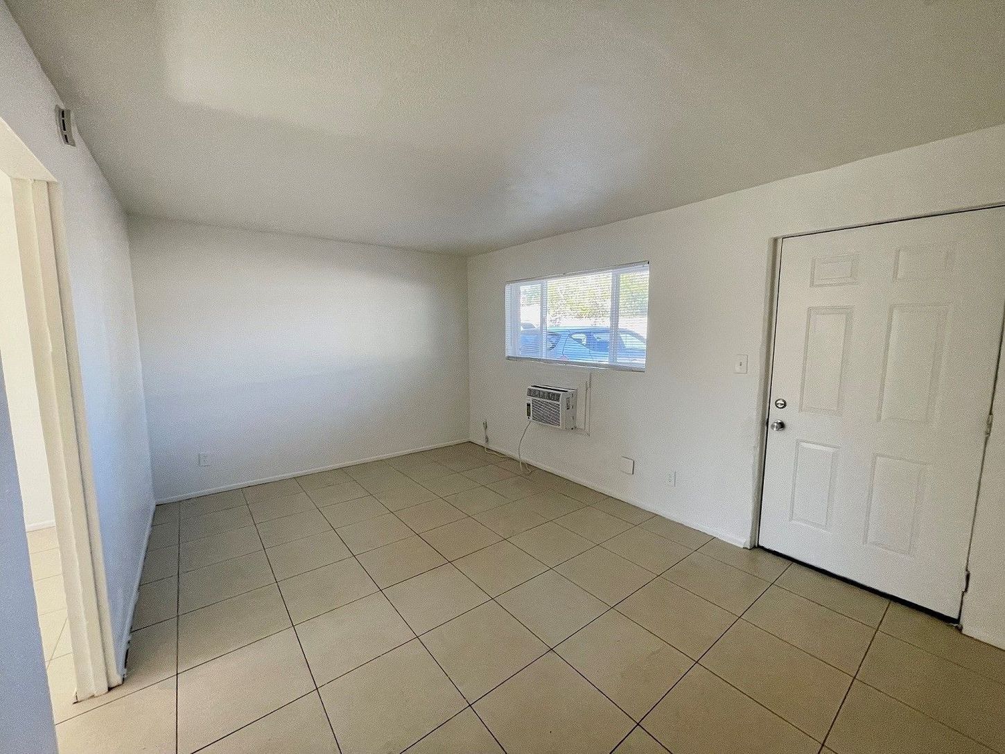 Empty room with tiled floor, white walls, a window, door, and air conditioner.