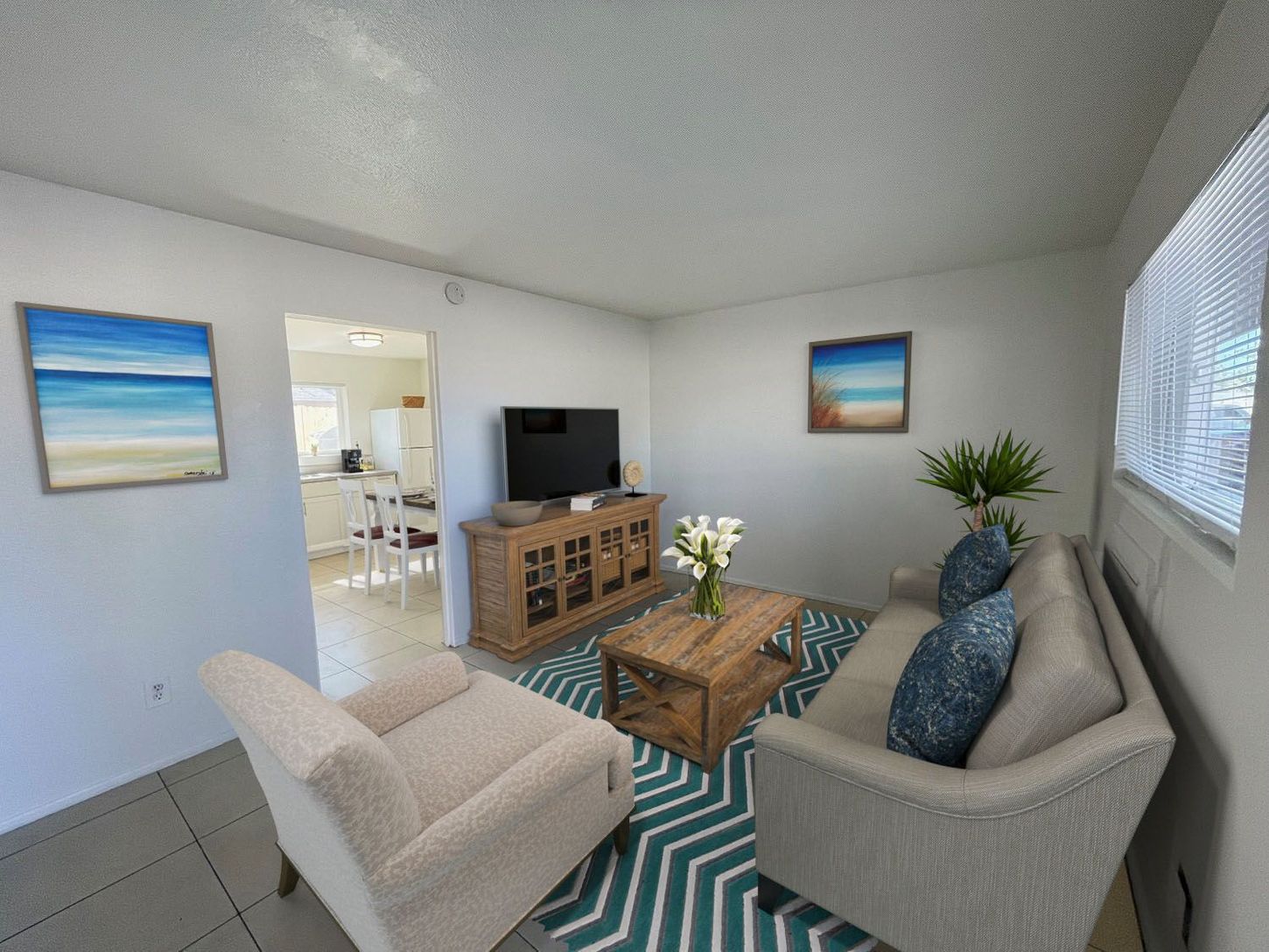 Living room with neutral furniture, ocean art, TV, and patterned rug.