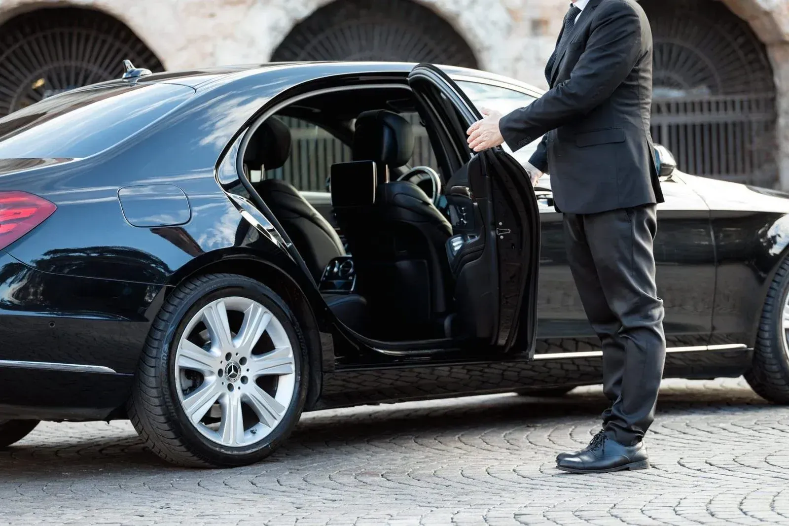 A man in a suit is opening the door of a black car.