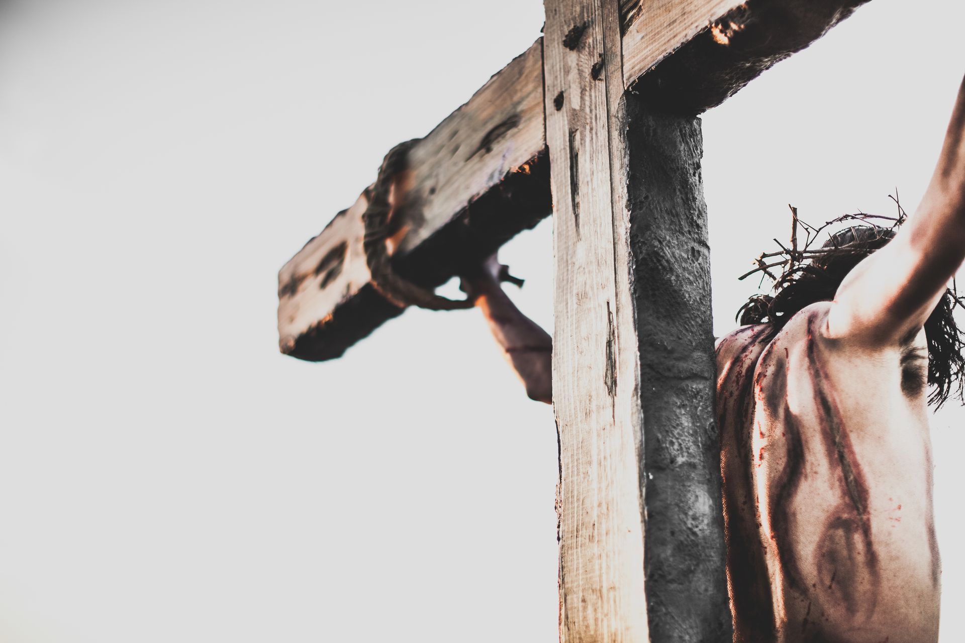 Close-up of a crucifix with Jesus’ outstretched arms against a bright background
