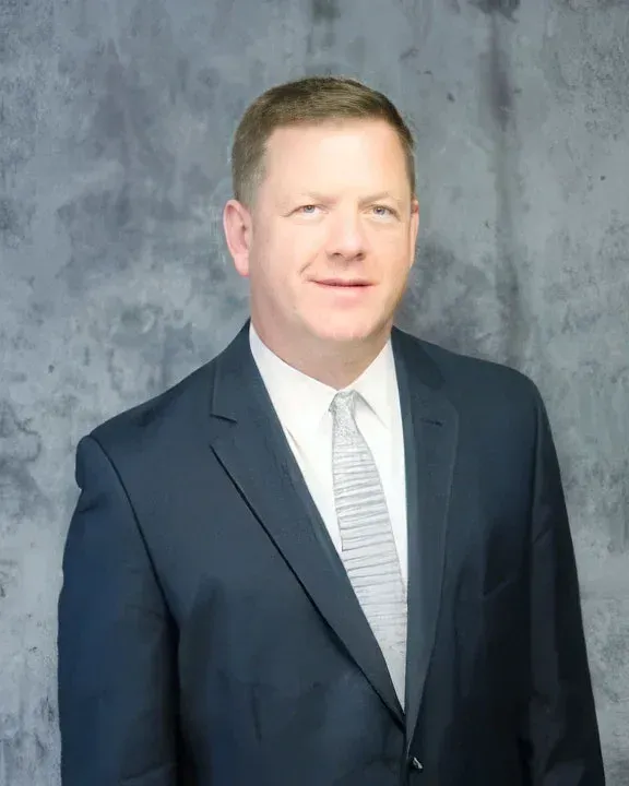 Man in a dark suit and white tie posing against a gray studio backdrop
