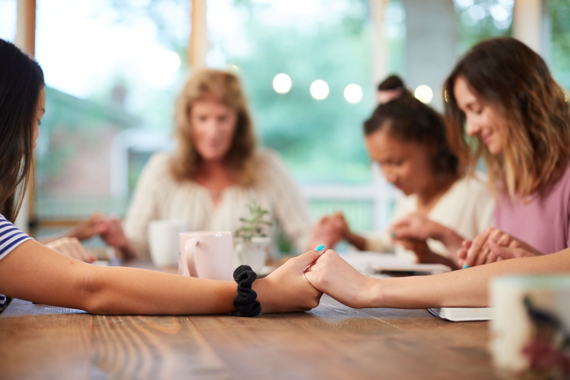 People seated around a table, hands clasped in a group discussion with notebooks and cups nearby