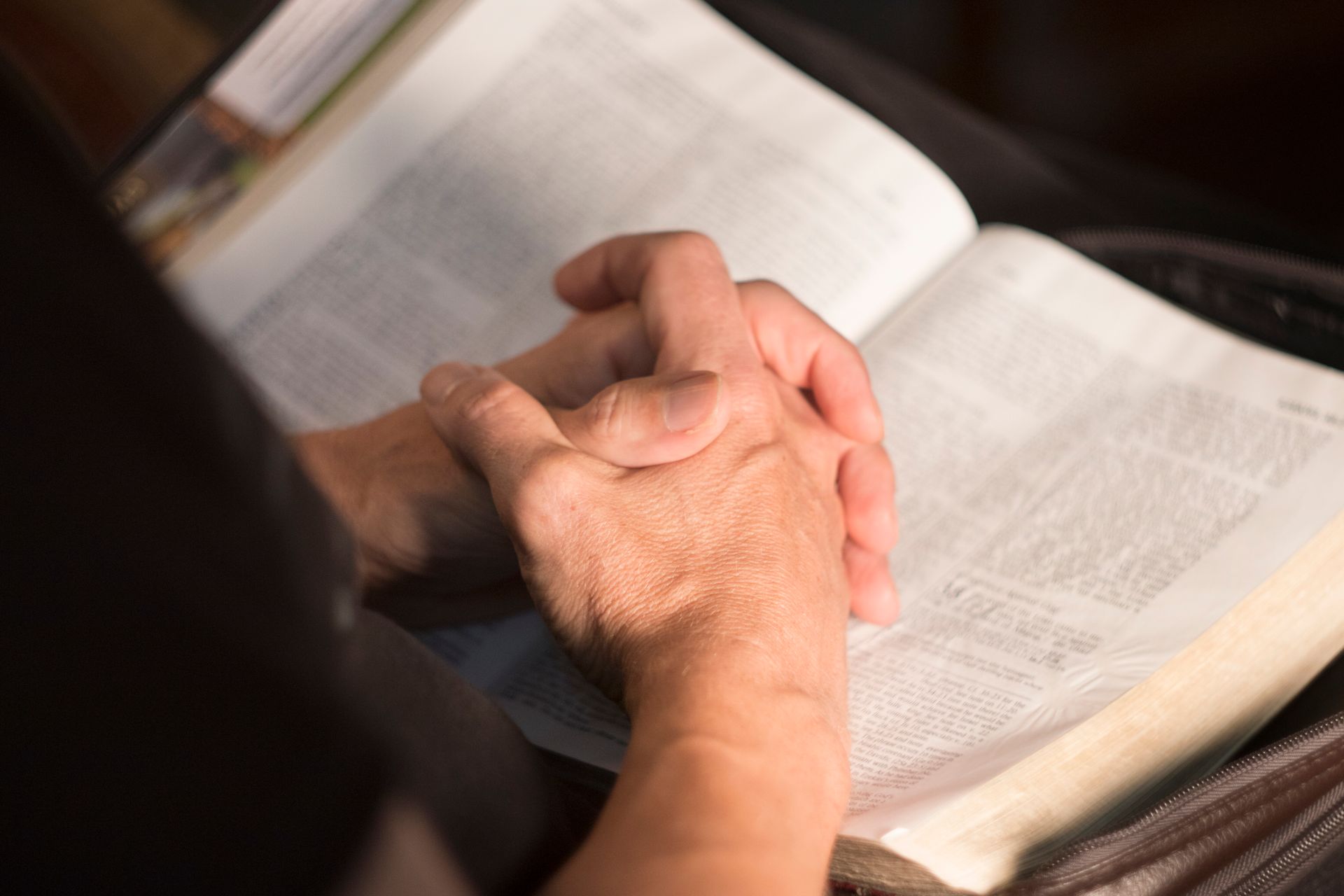 Hands clasped in prayer over an open Bible.