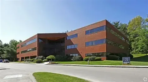 Brick office building with dark windows, surrounded by trees and a paved driveway under a clear sky
