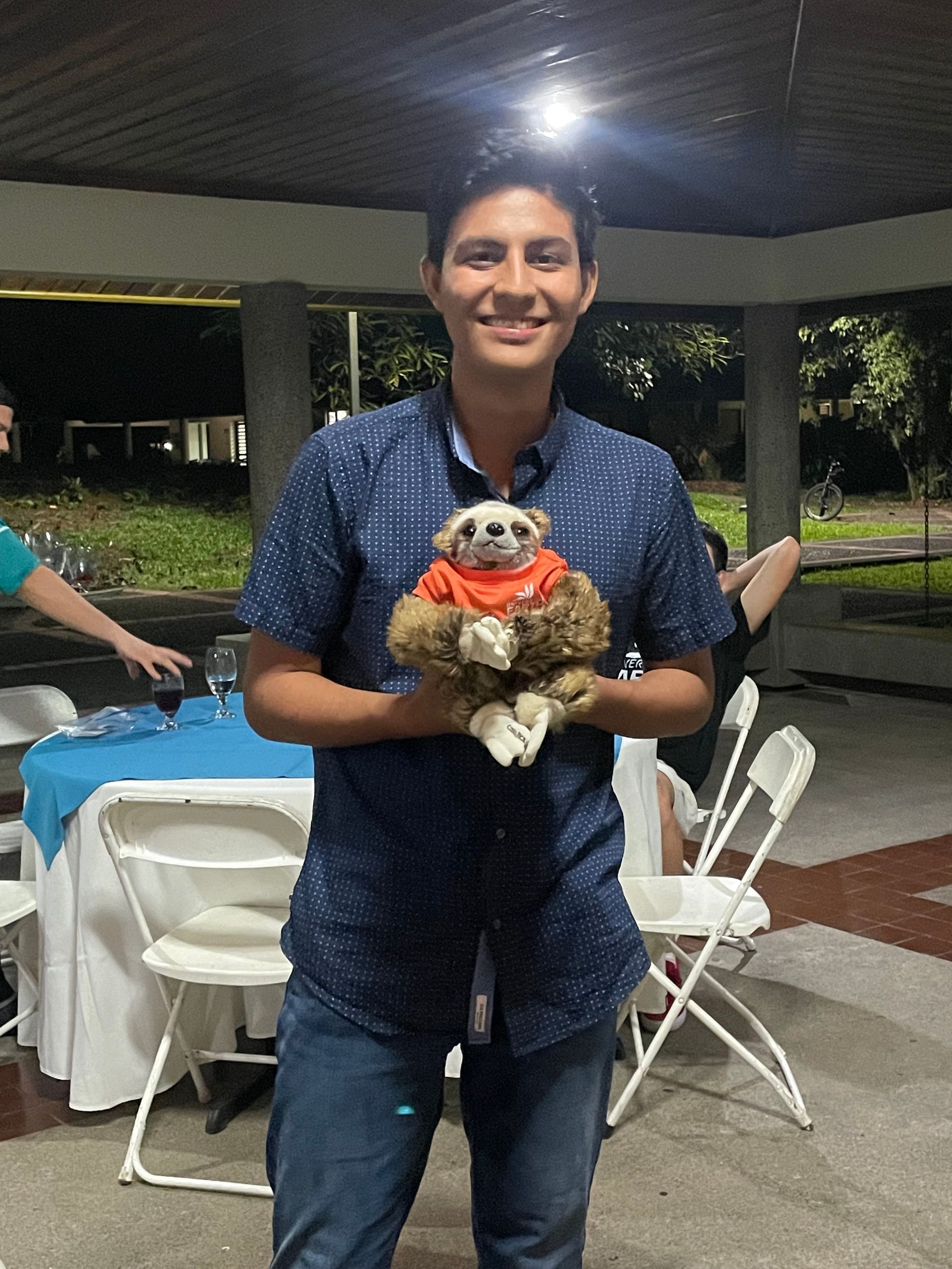 Un hombre con una camisa azul sostiene un perezoso de peluche.