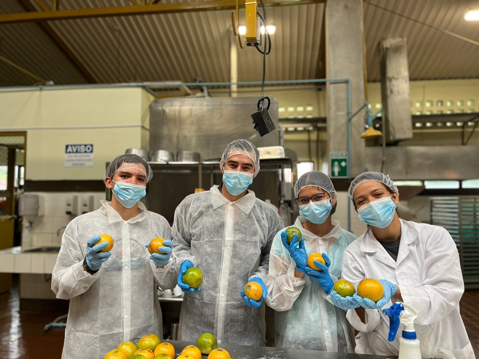 Un grupo de personas con máscaras y guantes sostienen naranjas en una cocina.
