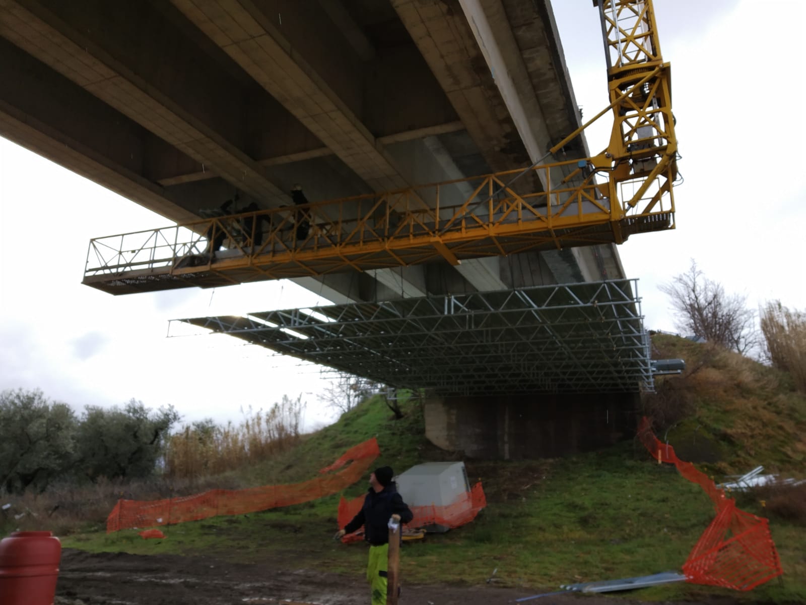 Cantiere con un ponte in riparazione. Un'impalcatura sostiene la parte inferiore del ponte. Una persona è in piedi nelle vicinanze.