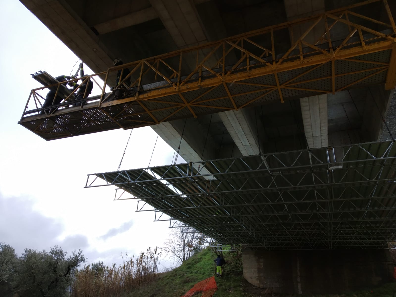 Operai su impalcature sotto un ponte di cemento, impegnati nella riparazione o nell'ispezione.