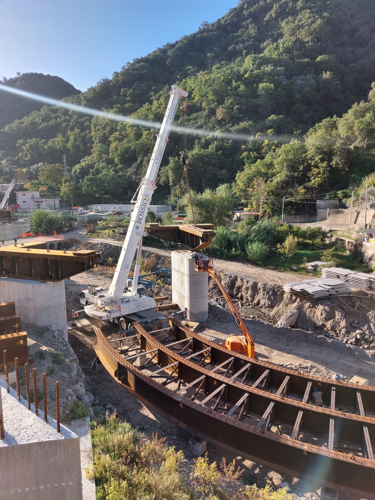 Una gru solleva una grande trave d'acciaio in un cantiere edile in una valle di montagna.