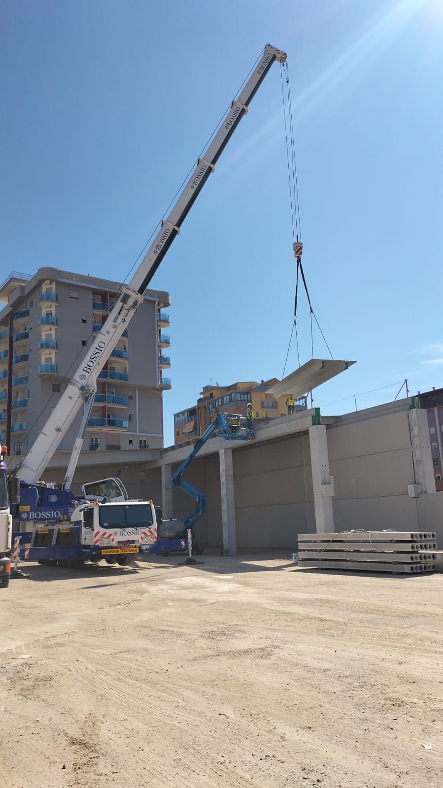 Una grande gru sta sollevando un pezzo di cemento davanti a un edificio.