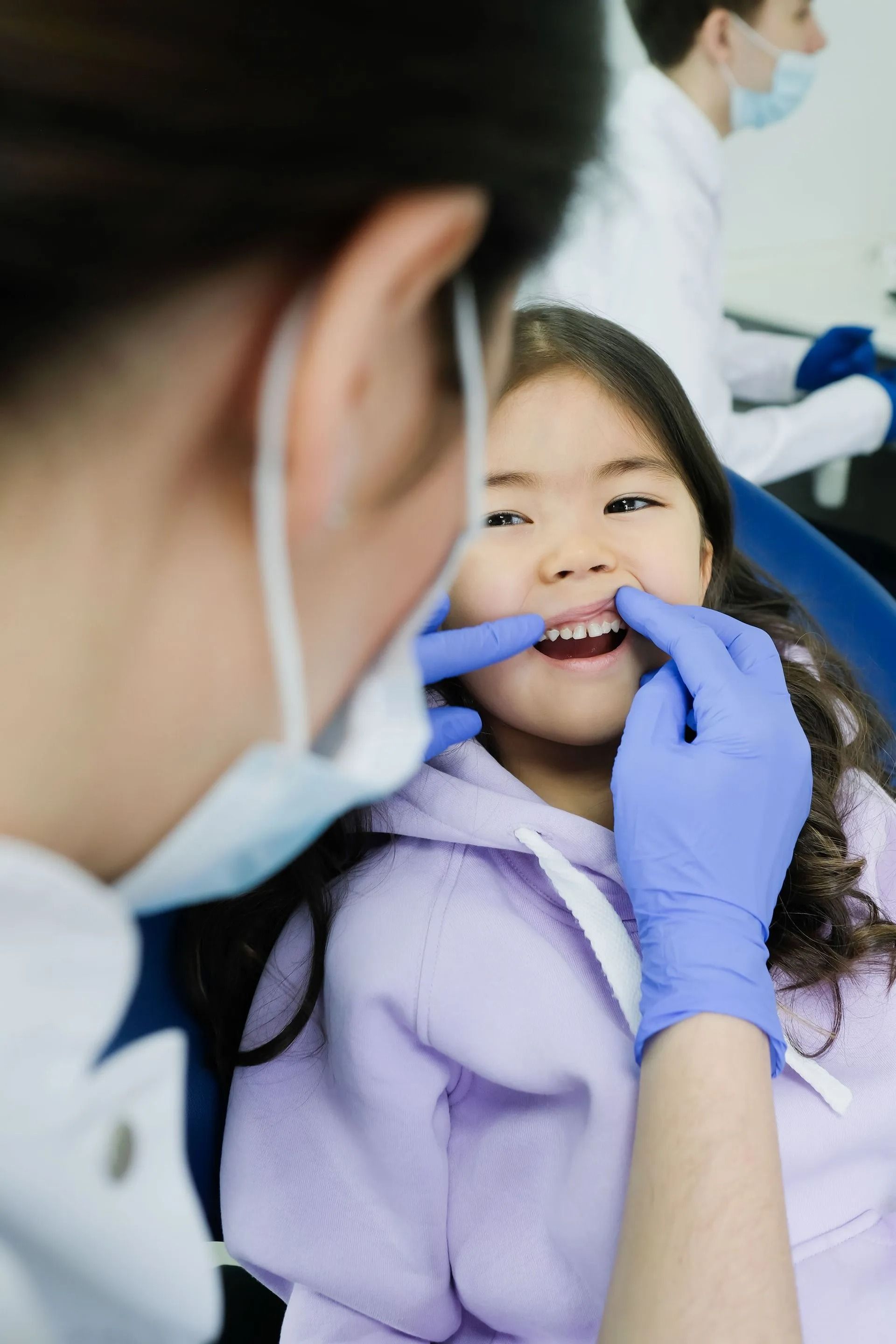 A dentist in a white coat and mask performs a dental procedure on a patient in a chair.