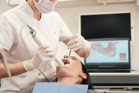A dentist and assistant in blue scrubs wearing masks perform a checkup on a patient lying in a dental chair.