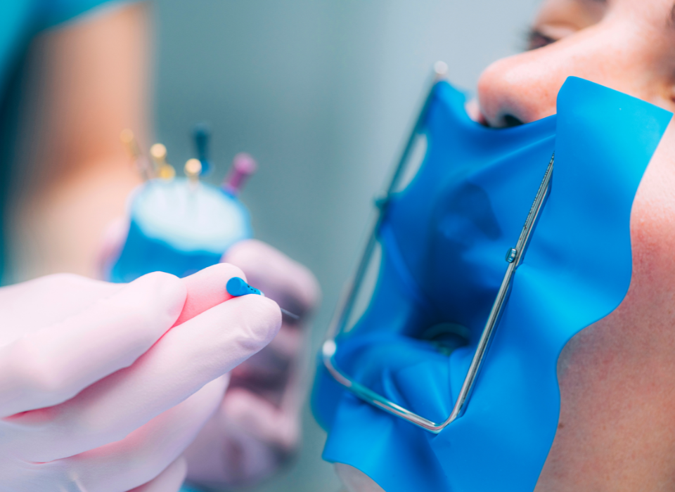 A dentist and assistant in blue scrubs wearing masks perform a checkup on a patient lying in a dental chair.