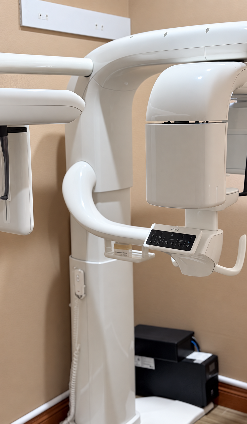Dental X-ray machine with white curved arm and control panel in a clinic room